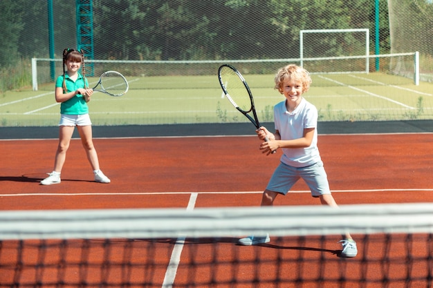 Jongen en meisje voelen zich vrolijk tijdens het buiten tennissen