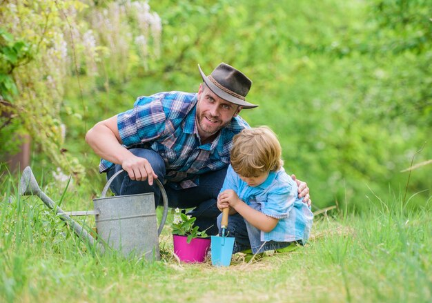 Jongen en vader in de natuur met gieter. Tuin gereedschap. Bloemen planten. Papa leert kleine zoon zorgplanten. Kleine helper in de tuin. Maak de planeet groener. Planten kweken. Zorg voor planten.