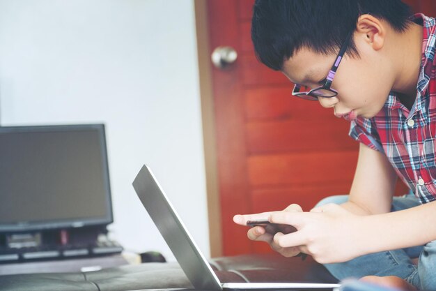 Jongen gebruikt mobiele telefoon en laptop terwijl hij thuis op bed zit