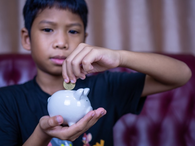 Jongen geld besparen in een wit varken spaarvarken. Besparing concept. Sparen voor de toekomst.