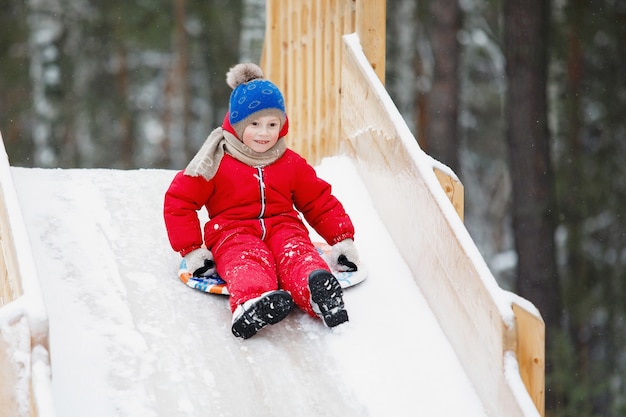 Jongen glijdt van een ijzige houten heuvel af op een besneeuwde dag.