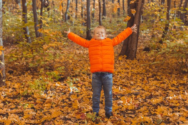 Jongen gooit gevallen bladeren op een achtergrond van herfstlandschap. Jeugd, herfst en natuur concept.