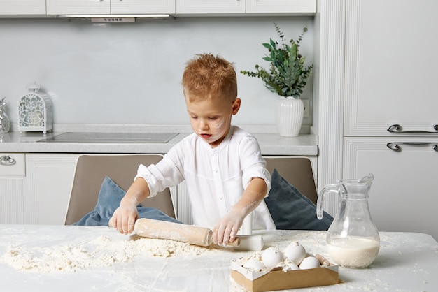 Jongen heeft plezier met het koken van deeg in een witte keuken