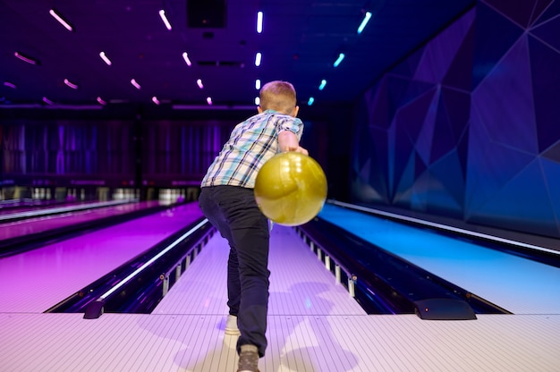 Jongen houdt een bal bij de baan in de bowlingbaan. Kid bereidt zich voor om een staking te scoren. Kinderen hebben plezier in het entertainmentcentrum, bowler kid