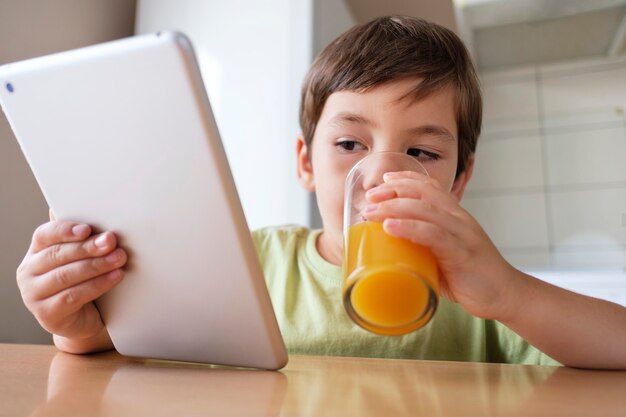 Jongen in de keuken sinaasappelsap drinken en kijken naar video op de tablet