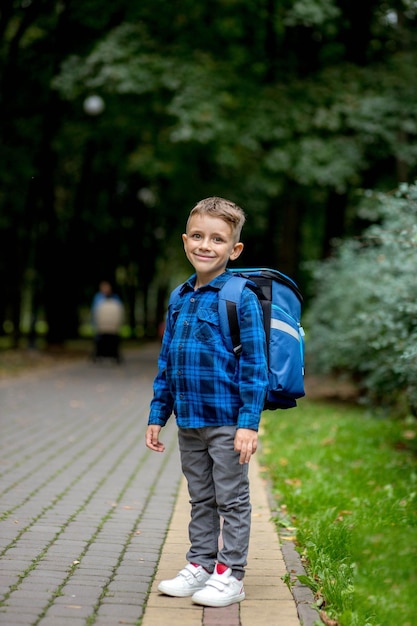 Jongen in de leerplichtige leeftijd met een blauwe rugzak gaat naar school in het park