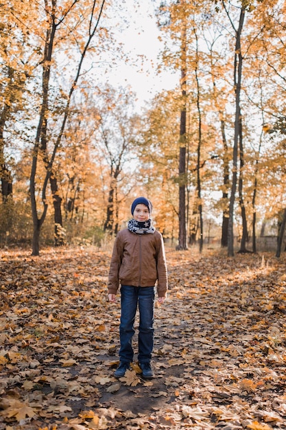 Jongen in een jas in de herfst in oranje bladeren in het park