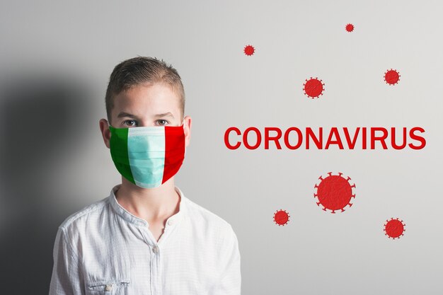 Jongen in een medisch masker met vlag van italië op zijn gezicht op lichte achtergrond.