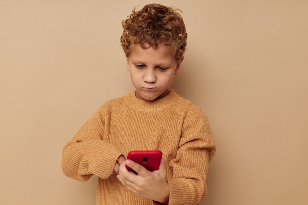 Jongen in een trui met een telefoon in zijn handen technologie beige achtergrond