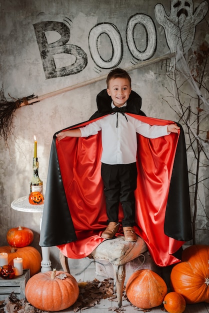 Jongen in een vampier Dracula kostuum Halloween staat tussen pompoenen