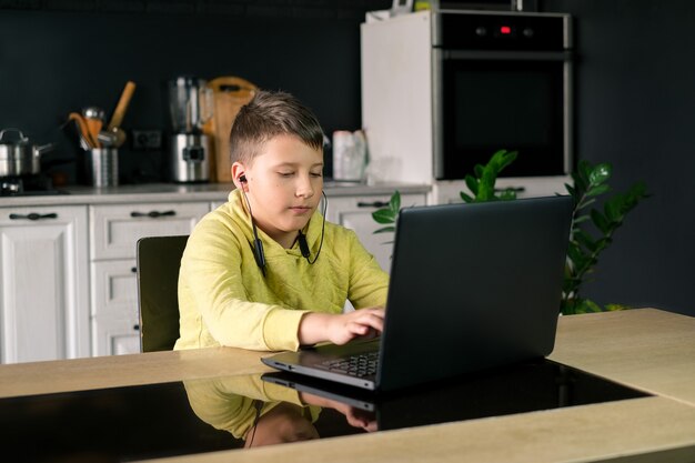 Jongen in gele kleding kijkt naar film die online studeert of een spel speelt op de computer in de keuken thuis