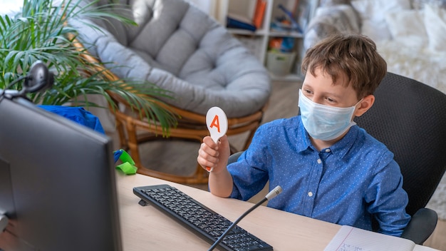 Jongen in gezichtsmasker met behulp van computer, huiswerk tijdens coronavirus quarantaine