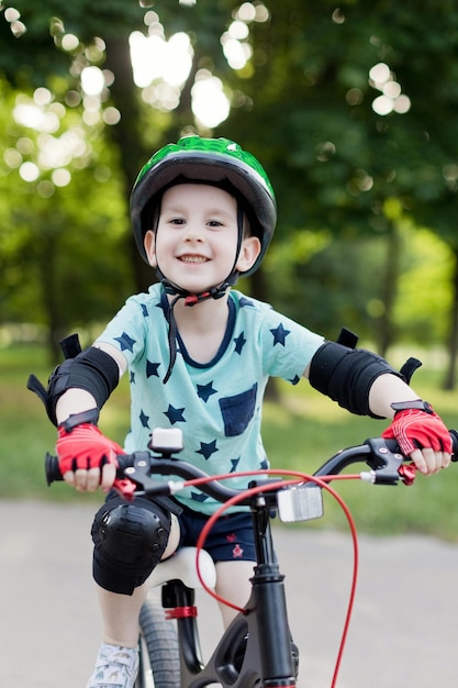 Jongen in groene helm rijden op zijn eerste fiets in het zomerpark