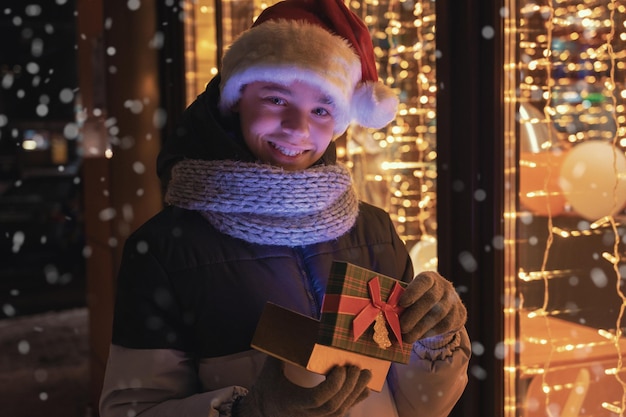 Jongen in kerstmuts met cadeaudoos kijkt en droomt