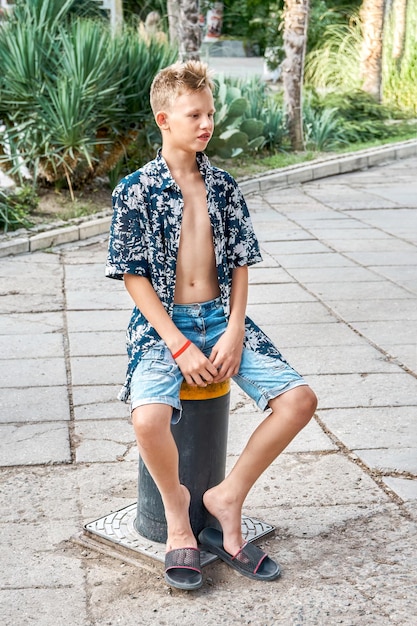 Foto jongen in shirt met bloemmotief en spijkerbroek zit op automatische hefpaal op straat in de stad