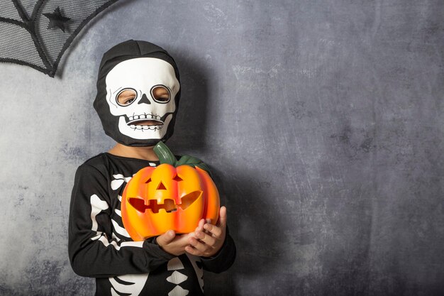 Foto jongen in skelet kostuum met jack o lantaarn tegen grijze muur