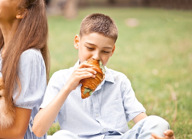 Jongen jongen zittend op picknick zomervakantie en versgebakken croissantsandwich eten.