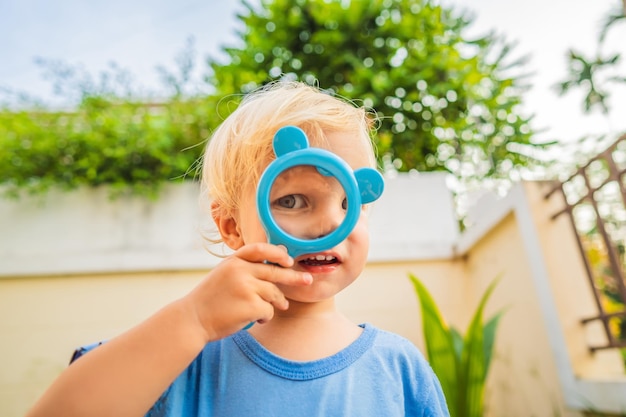 Jongen kijkt in een vergrootglas tegen de achtergrond van de tuin Thuisonderwijs