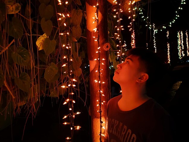 Foto jongen kijkt's nachts naar verlichte kerstverlichting.