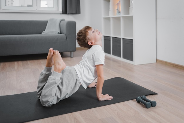 Jongen-kind doet fitness, yoga thuis in de woonkamer. Gezondheidsbevordering.