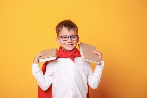 Jongen kind schooljongen met bril hol boek in zijn handen in een superheld kostuum op gele achtergrond