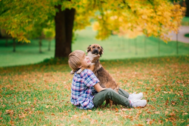 Jongen knuffelen een hond en spelen met in de herfst, stadspark