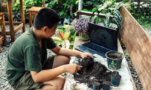 Jongen leert bloemen in potten telen door online les te geven over aarde in potten scheppen