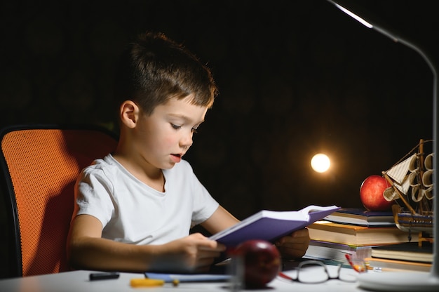 Jongen leert lessen in de thuisomgeving aan tafel in het licht van een tafellamp.