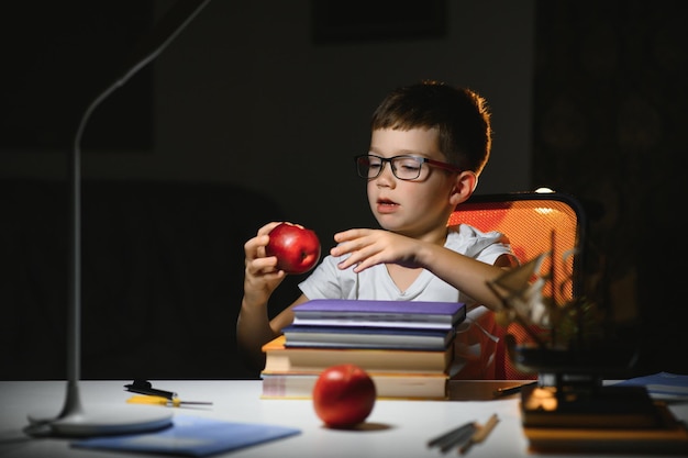 Jongen leert lessen in de thuissituatie aan tafel in het licht van een tafellamp.