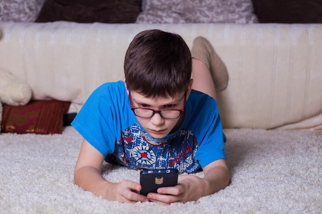 Jongen liggend met smartphone op een tapijt thuis