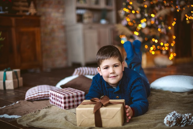 Jongen ligt op de vloer voor de kerstboom en houdt een geschenk in zijn handen