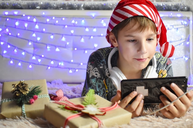 Jongen ligt op het bed met dozen met geschenken met laptop