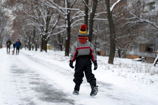 Jongen loopt in het winterpark. Kind loopt langs besneeuwde weg. Achteraanzicht