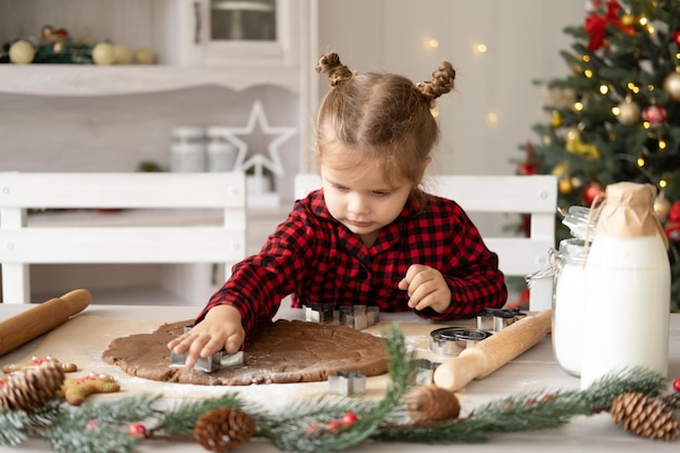 jongen meisje in rode pyjama feestelijke peperkoek koken in kerst ingerichte keuken. kerstkoekjes