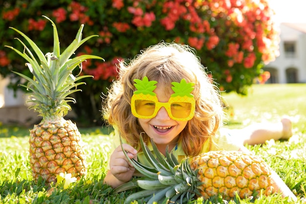 Jongen met ananas op hoofd speelt met vers tropisch fruit buitenshuis opgewonden grappig kind kind gezicht wi...