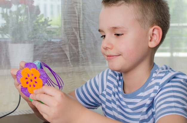 Jongen met behulp van 3d-pen. gelukkig kind dat bloem van gekleurd abs plastic maakt