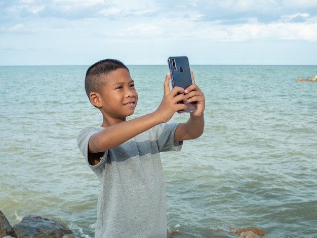 Jongen met behulp van een telefoon om een selfie te maken op de achtergrond van een zee