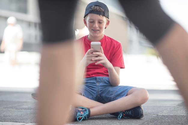 Jongen met behulp van slimme telefoon, zittend op een skateboard
