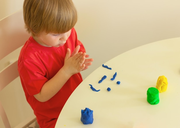 Jongen met blond haar en in een rood shirt beeldhouwt uit plasticine kindertijd ontwikkelingsactiviteiten voor kinderen