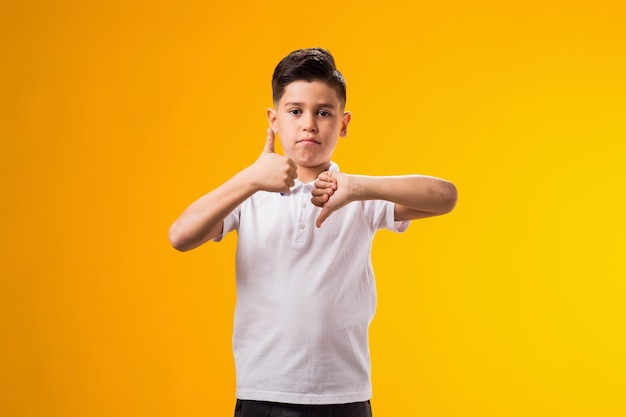 Foto jongen met duim omhoog en duim omlaag gebaar op gele achtergrond