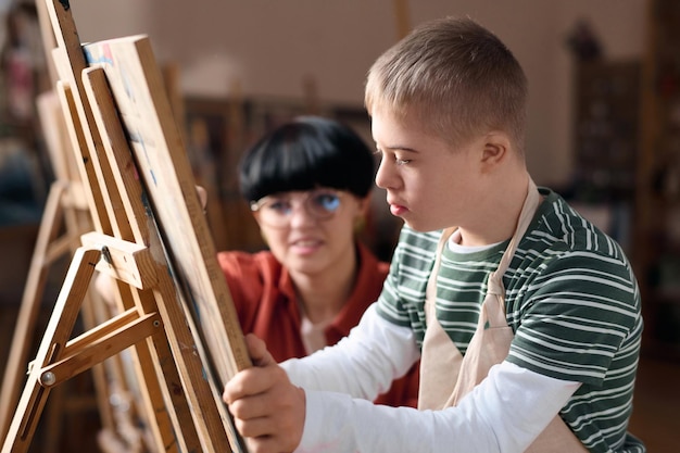 Foto jongen met een handicap schildert op een easel in de kunstles