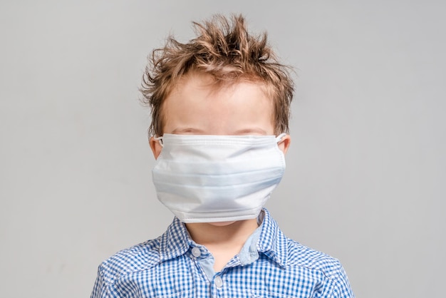 Jongen met een medisch masker op haar gezicht op een grijze achtergrond geïsoleerd