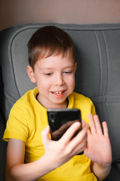 Foto jongen met een mobiele telefoon spreekt thuis via videobellen de schooljongen communiceert via een videoverbinding videochatten thuis