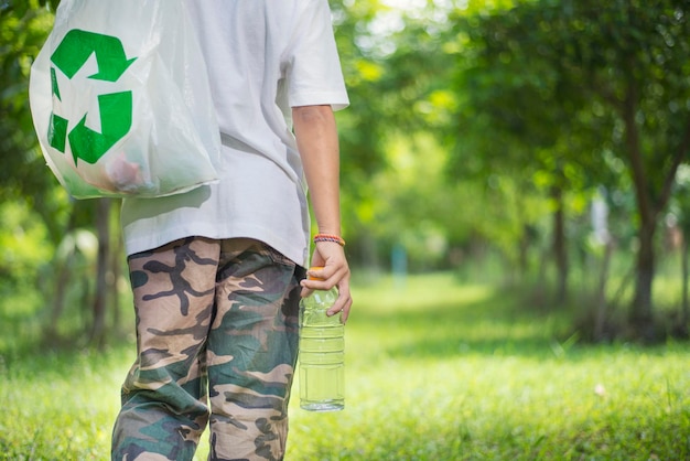 Jongen met een plastic fles in zijn hand en draagt vuilniszak Onder het groene bos Close-up