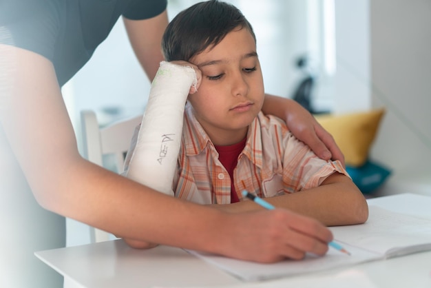 Jongen met gebroken arm in gips met hulp van oudere broer voor huiswerk foto van hoge kwaliteit