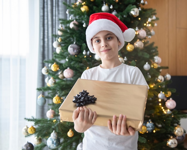 Jongen met geschenken speelt in de buurt van de kerstboom. Woonkamer interieur met kerstboom en versieringen. Nieuwjaar. Cadeaus geven.