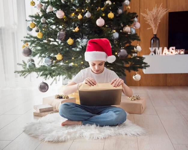 Jongen met geschenken speelt in de buurt van de kerstboom. Woonkamer interieur met kerstboom en versieringen. Nieuwjaar. Cadeaus geven.