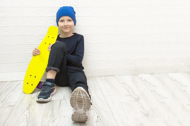 Jongen met hoed zit op de vloer bij de muur met een skateboard in zijn handen actieve levensstijl