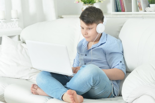 Jongen met hoofdtelefoon die laptop thuis gebruikt