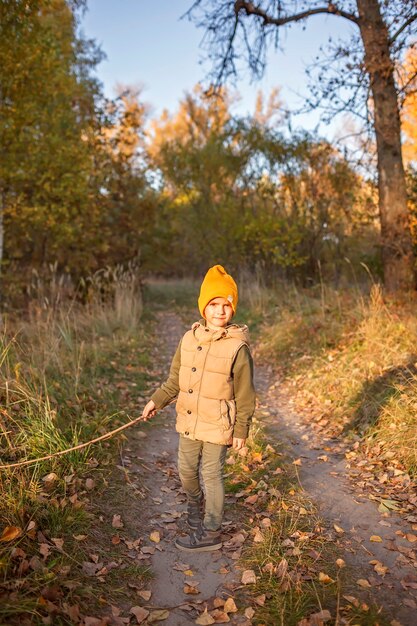 Jongen met houten stok loopt door het pad en verkent het prachtige bos tijdens herfstwandeling